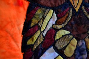 Multi-colored applique feathers edged with black thread on an owl panel