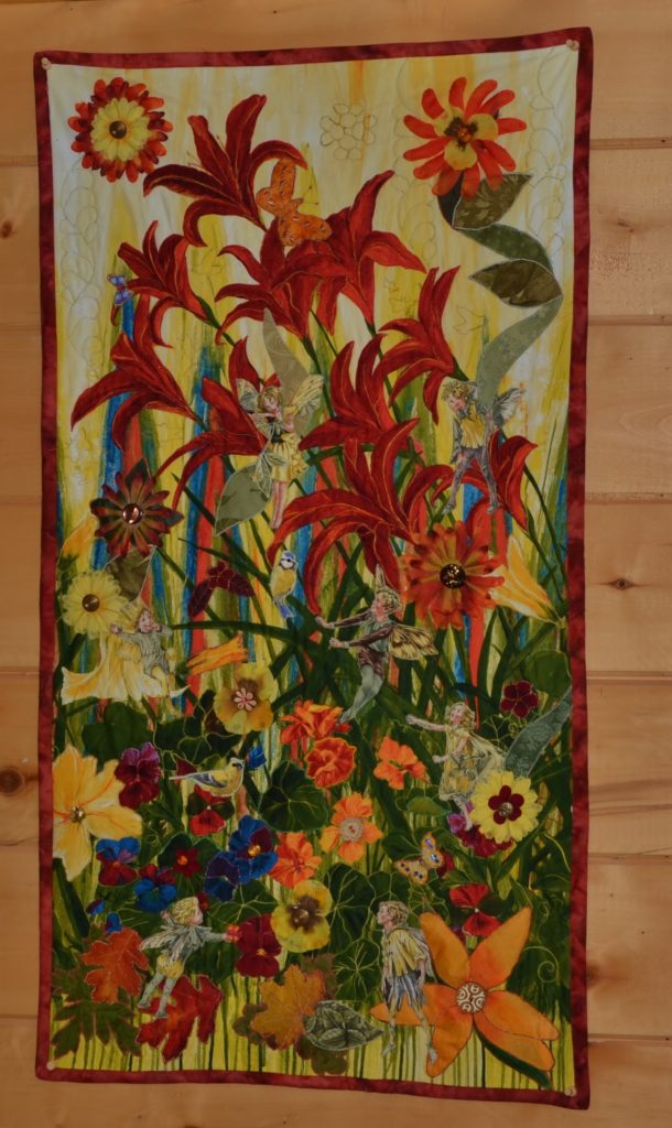 An appliqued panel showing orange lilies, autumn grasses, and fairies and flowers hidden in it