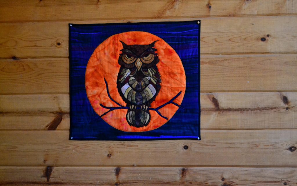 An elaborately appliqued "mosaic" owl sits in front of an orange harvest moon - wall hanging quilt panel