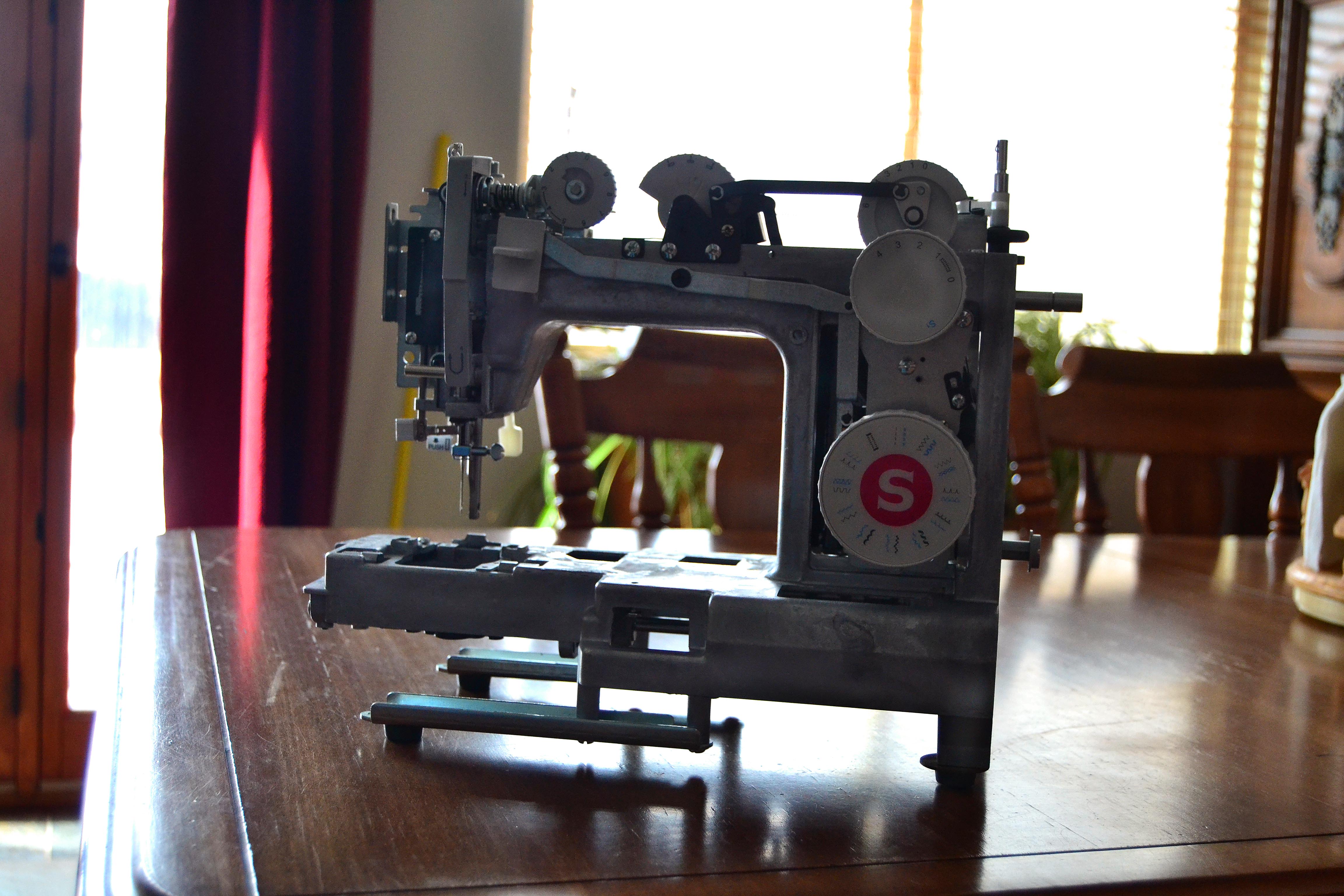 A sewing machine that's been stripped down to it's metal frame on a kitchen table in front of a window
